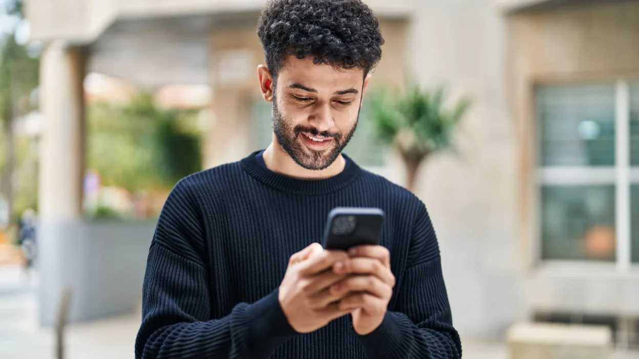 Man smiling while selecting a custom phone number on his smartphone using NY Mobile